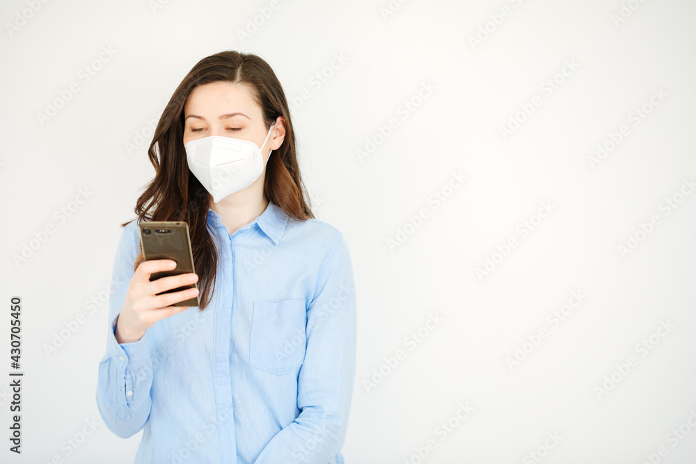 Young woman wears a ffp2 protective mask and looks at something on a cell phone. Work in the office with ffp2 protective mask. Wearing mask in office Young woman wears a ffp2 protective mask and looks at something on a cell phone. Work in the office with ffp2 protective mask. Wearing mask in office