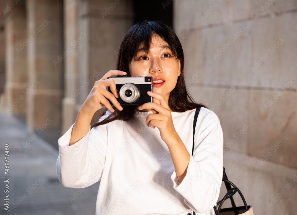 Young chinese girl is taking photos on her camera while journey through the city. High quality photo