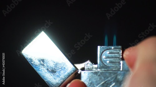 Silver Zippo lighter ignites in front of black background. Lighter close up. Slow motion. photo