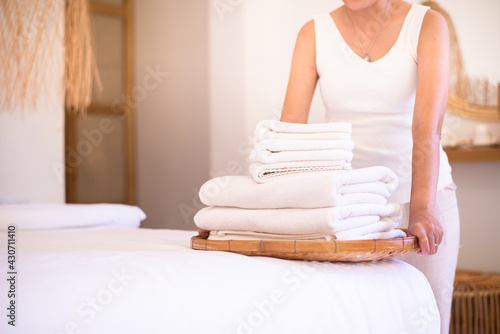Maid woman putting stack clean towels white color on bed in hotel