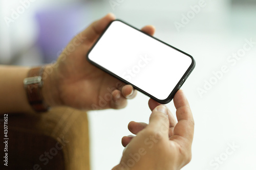 Male holding smartphone with horizontal mock-up screen in blurred background