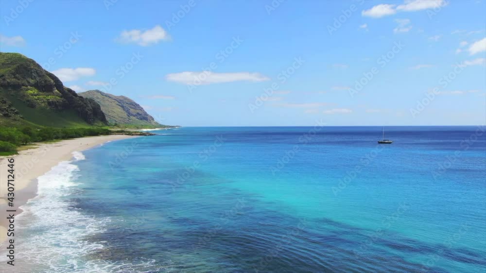 Drone shot of a beautiful beach in Hawaii and a sailboat. Secluded white sand beach. Crystal blue ocean water with green lush mountains. West side of Oahu, Hawaii. Drone shot of a beautiful beach in Hawaii and a sailboat. Secluded white sand beach. Crystal blue ocean water with green lush mountains. West side of Oahu, Hawaii.