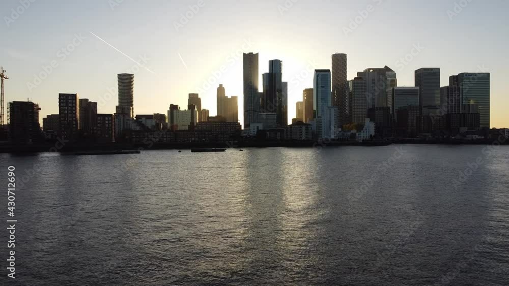 Aerial drone flight over River Thames showing silhouette of skyscraper buildings in Canary Wharf District of London during sunrise. Aerial drone flight over River Thames showing silhouette of skyscraper buildings in Canary Wharf District of London during sunrise.