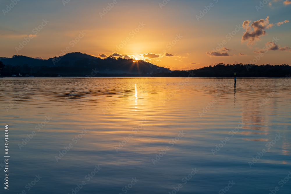 Sunrise waterscape with scattered clouds and sun rays