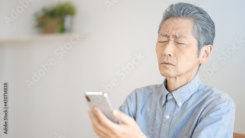 スマートフォンを使う老眼のシニア男性 © aijiro