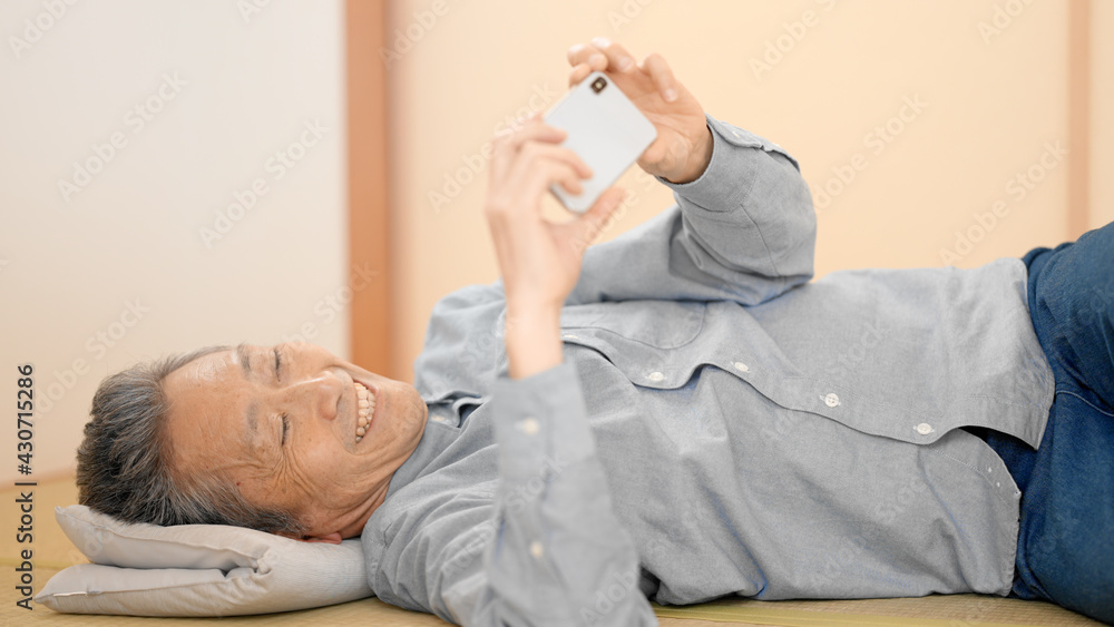寝っ転がりながらスマートフォンを見るシニア男性 寝っ転がりながらスマートフォンを見るシニア男性