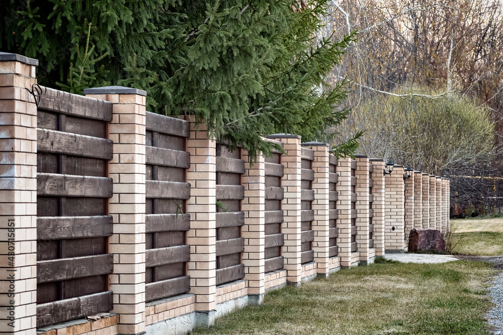 A fence around the territory of a private house made of bricks and boards. A fence around the territory of a private house made of bricks and boards.