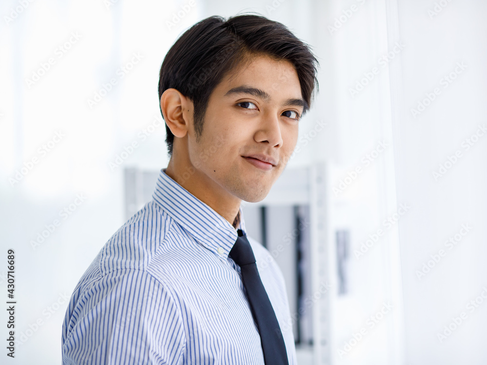 Portrait shot of Asian young happy successful businessman take black formal jacket uniform off and stand smiling in front white bookshelf background alone in library Portrait shot of Asian young happy successful businessman take black formal jacket uniform off and stand smiling in front white bookshelf background alone in library