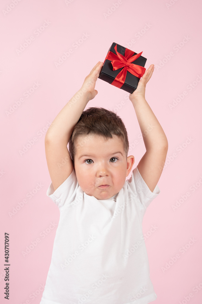 Cute little boy holding wrapped present over his head on pink background Cute little boy holding wrapped present over his head on pink background