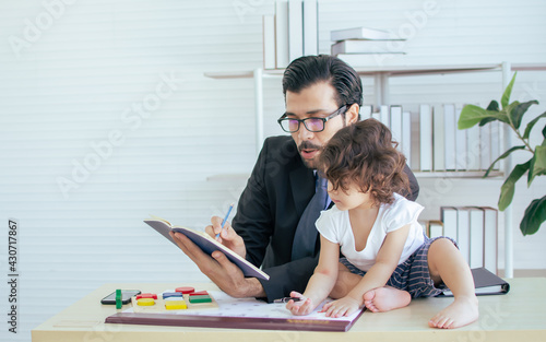 Caucasian beard handsome father wearing eyeglasses, formal suit, teaching of writing and reading, taking care of his little curly hair daughter while working in indoor office or workplace.