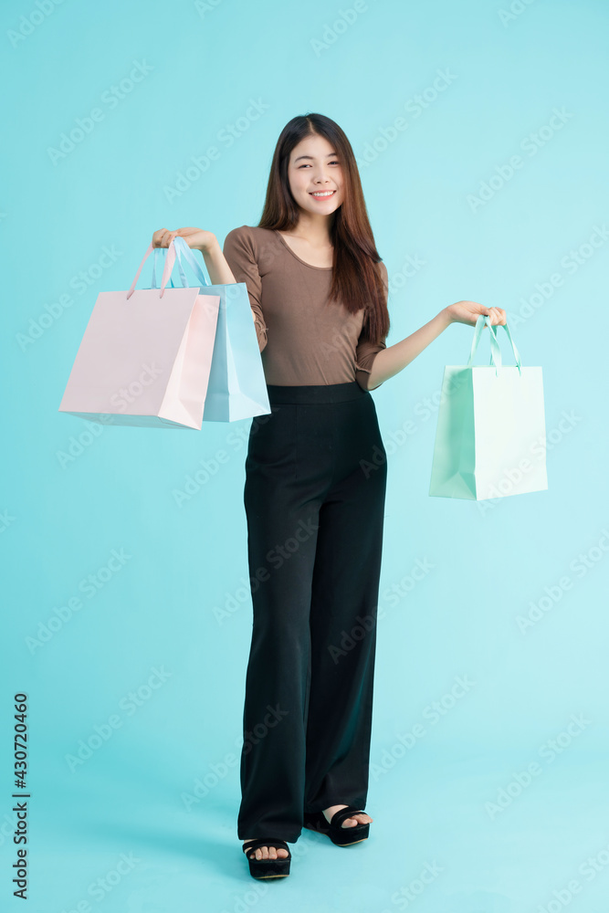 portrait of cheerful young brunette asian teen woman holding  shopping bags over Blue background.