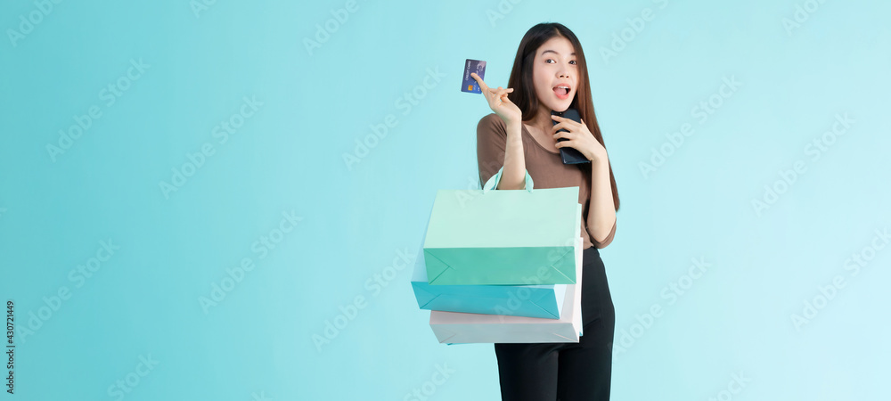 portrait of cheerful young brunette asian teen woman holding shopping bags , smartphone and credit card over Blue background. Shopaholic shopping Fashion concept. portrait of cheerful young brunette asian teen woman holding shopping bags , smartphone and credit card over Blue background. Shopaholic shopping Fashion concept.