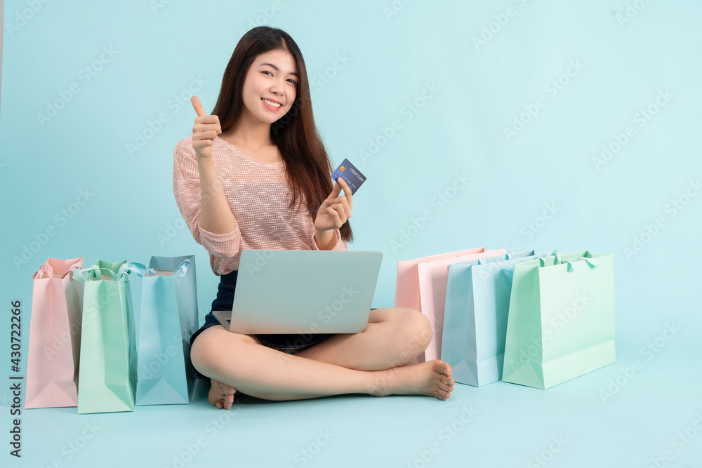 Online Order. Asian girl sitting with laptop using credit card shopping online on blue background, shopping online concept Online Order. Asian girl sitting with laptop using credit card shopping online on blue background, shopping online concept