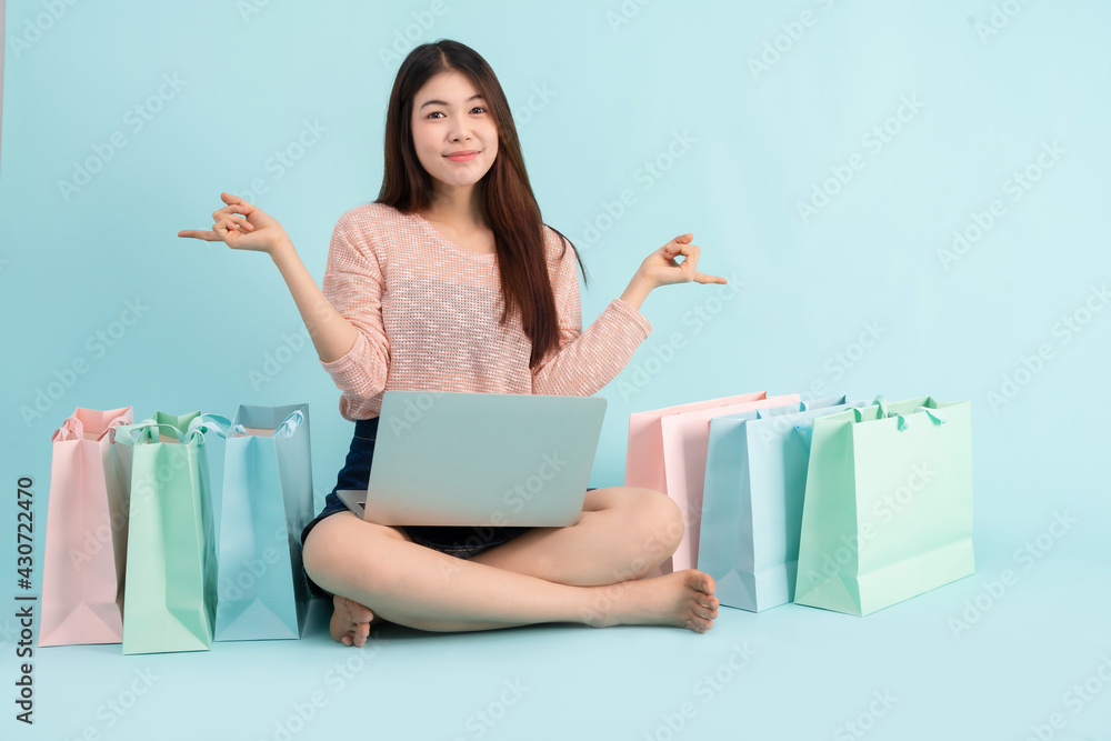 Online Order. Asian girl sitting with laptop using credit card shopping online on blue background, shopping online concept Online Order. Asian girl sitting with laptop using credit card shopping online on blue background, shopping online concept