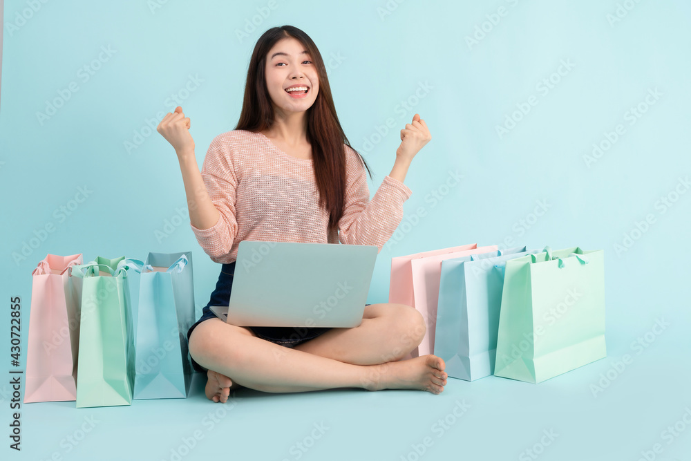 Online Order. Asian girl sitting with laptop using credit card shopping online on blue background, shopping online concept Online Order. Asian girl sitting with laptop using credit card shopping online on blue background, shopping online concept