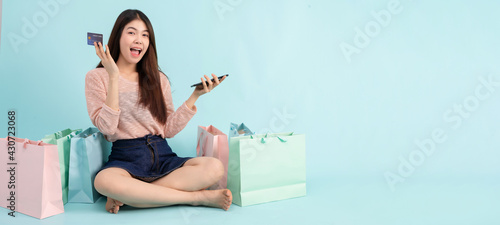 Online Order. Asian girl sitting with smart phone using credit card shopping online on blue background, shopping online concept