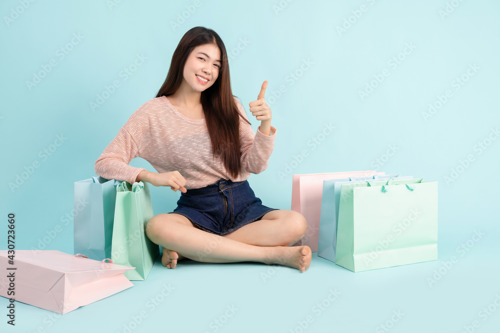 Online Order. Asian girl sitting with shopping bag on blue background, shopping online concept Online Order. Asian girl sitting with shopping bag on blue background, shopping online concept
