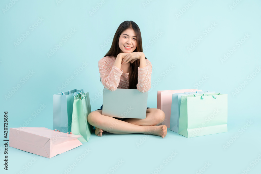 Online Order. Asian girl sitting with shopping bag on blue background, shopping online concept Online Order. Asian girl sitting with shopping bag on blue background, shopping online concept