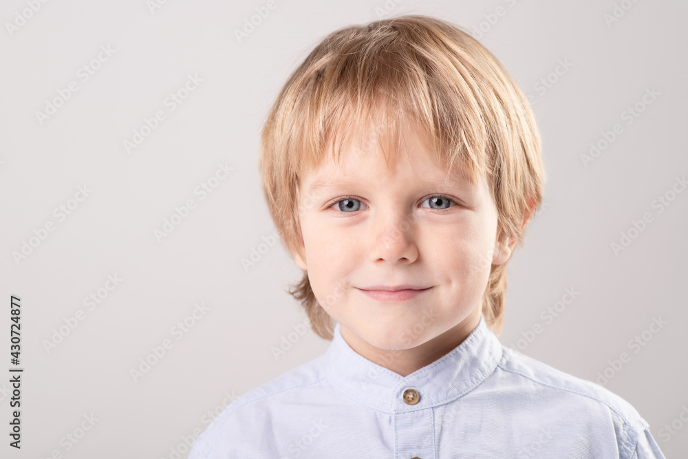Portrait of Caucasian child with blond hair, beautiful gray eyes. Casual clothing. Boy looks ahead confidently. Eye contact. Gray studio background. Healthy kid, childhood, personality concept. Portrait of Caucasian child with blond hair, beautiful gray eyes. Casual clothing. Boy looks ahead confidently. Eye contact. Gray studio background. Healthy kid, childhood, personality concept.