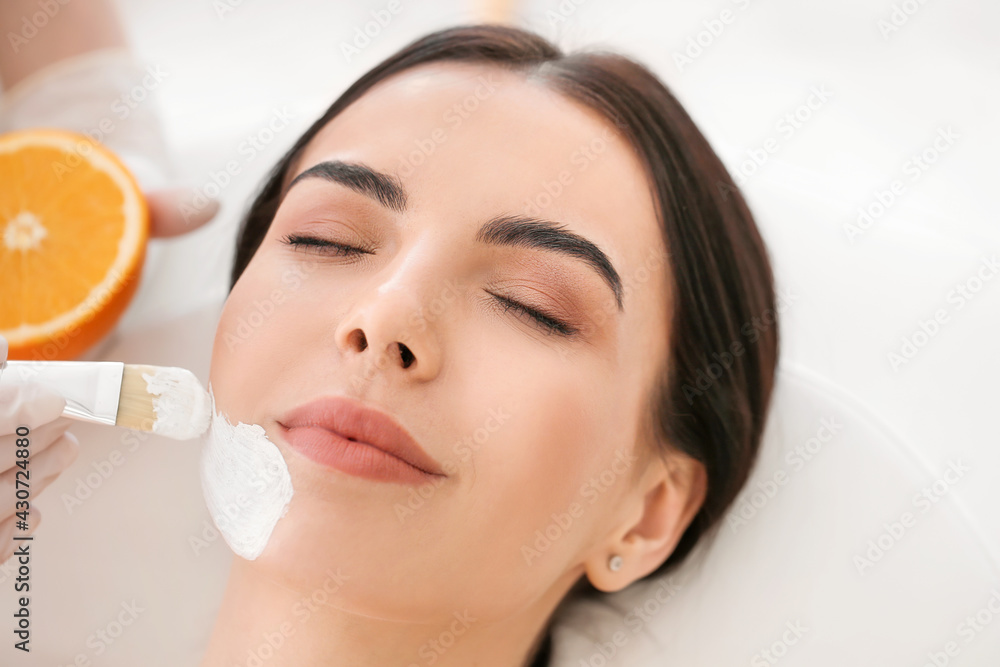 Cosmetologist applying mask on woman's face in beauty salon