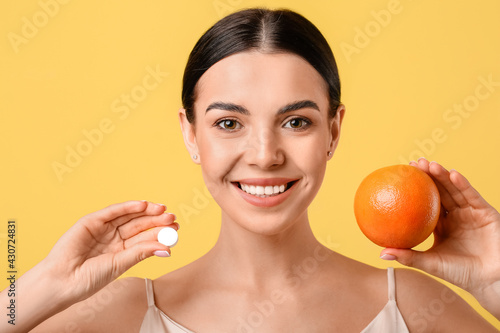 Beautiful woman with grapefruit and vitamin C pill on color background