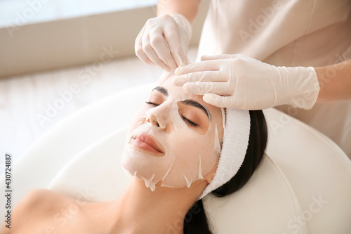 Cosmetologist applying sheet mask on woman's face in beauty salon photo