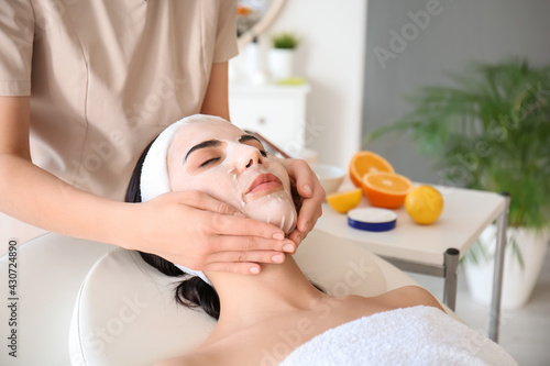 Cosmetologist applying sheet mask on woman's face in beauty salon