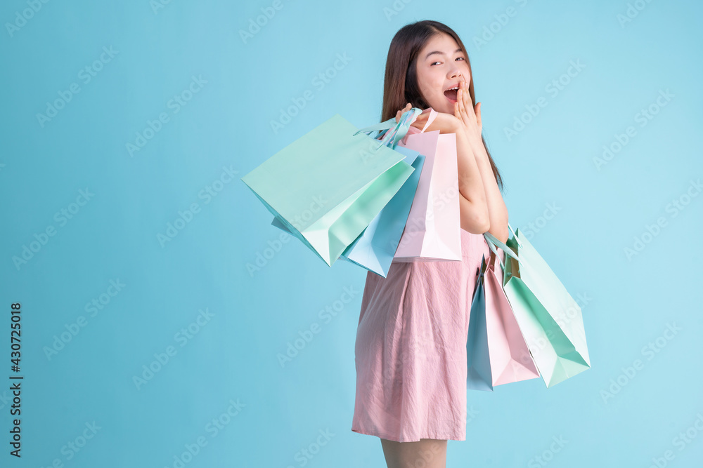 portrait of cheerful young brunette woman holding credit card and shopping bags over Blue background. shopaholic Concept