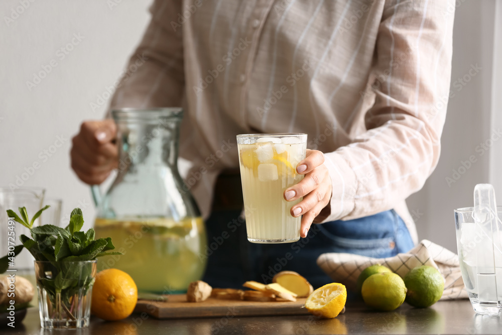 Woman with jug and glass of ginger lemonade in kitchen Woman with jug and glass of ginger lemonade in kitchen