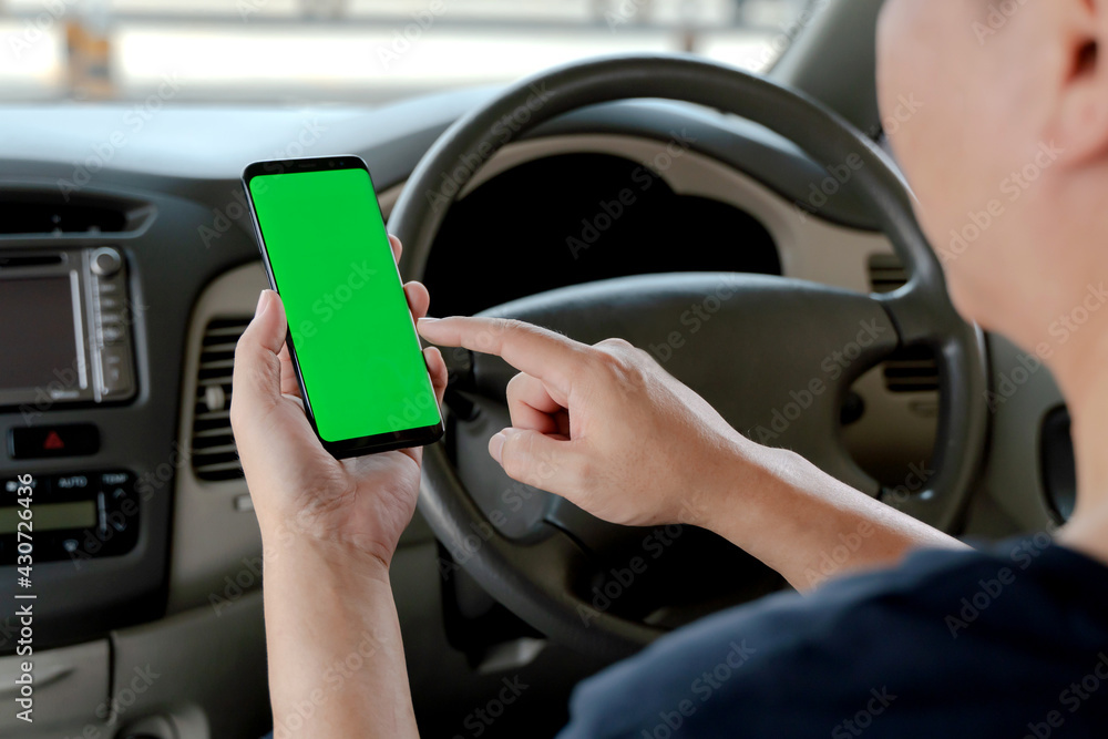 Mock up of man using mobile smart phone inside a car. Driver hand holding blank green screen smartphone, searching address and pin location via map navigator application, transportation