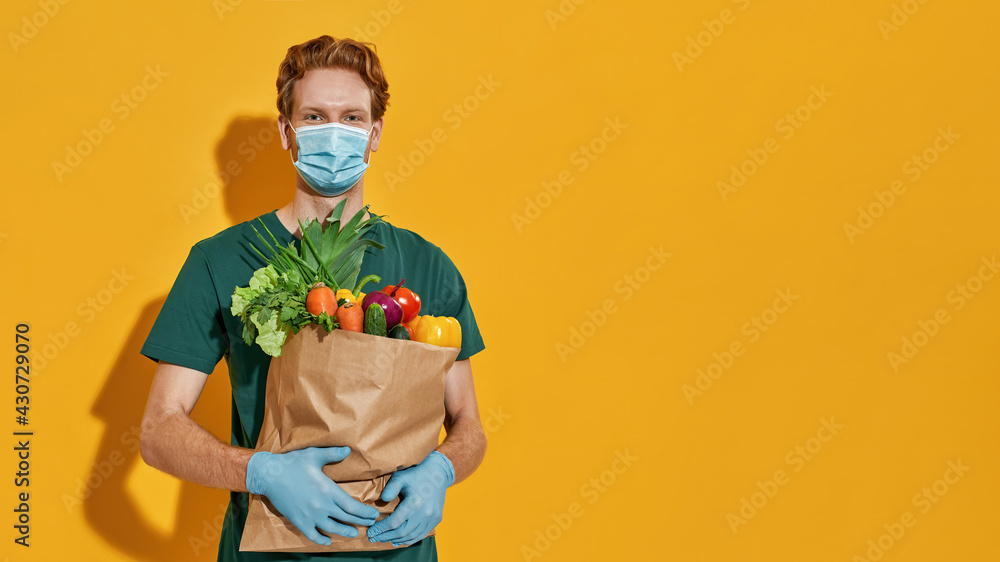Young courier in mask holding packet with green grocery Young courier in mask holding packet with green grocery