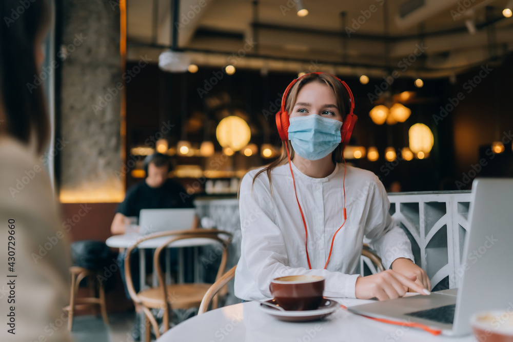 Fototapeta premium A girl sitting in a coffee shop with headphones. Coronavirus outbreak.