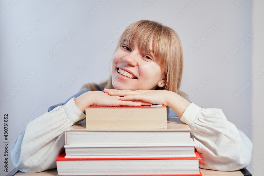 Young school girl with books in class with copy space. Attractive smiling blonde student relaxing lying on stack of books. Homeschooling or back to school concept. High quality photo Young school girl with books in class with copy space. Attractive smiling blonde student relaxing lying on stack of books. Homeschooling or back to school concept. High quality photo