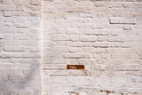 Red brick wall is plastered and painted white. Partially damaged. Light rustic background.