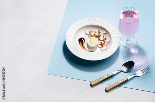 Fresh summer vitamin lunch of salad of radish, arugula, eggs with teriyaki sauce and rose sparcling wine with shadow in sunlight on white wood table, blue color. Food background in modern style.