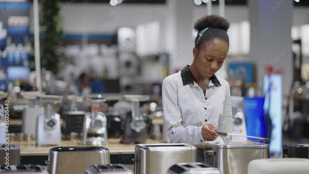 female shopper is examining toaster models in home appliances store, afro american lady is viewing exhibition samples female shopper is examining toaster models in home appliances store, afro american lady is viewing exhibition samples