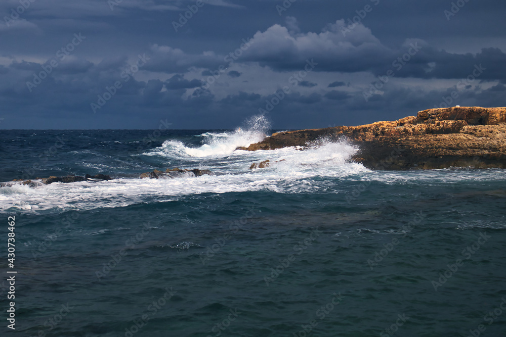 Sun shining on a rock as waves crash against it on a stormy day in Qawra, Malta.
