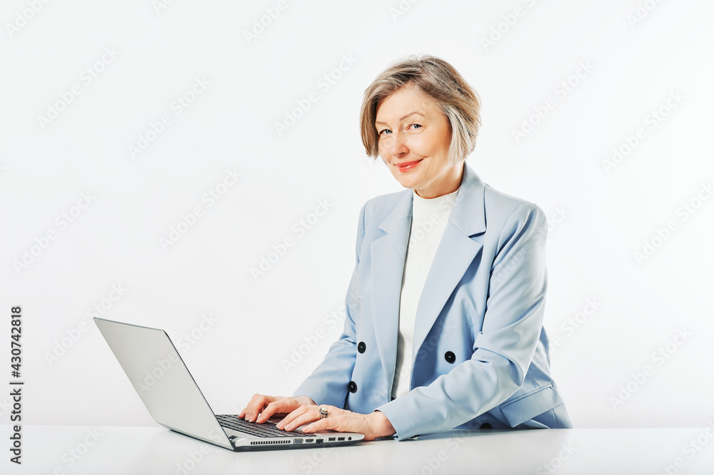 Studio portrait of middle age woman posing on white background, sitting at the desk, using laptop Studio portrait of middle age woman posing on white background, sitting at the desk, using laptop
