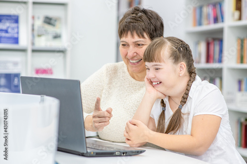 Foto Happy teacher and smiling girl with down syndrome use a laptop at library