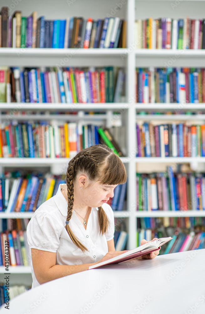 Girl with syndrome down reads a book at library. Education for disabled children concept. Empty space for text Girl with syndrome down reads a book at library. Education for disabled children concept. Empty space for text