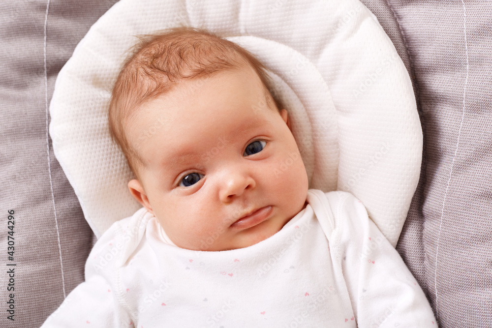 Charming adorable newborn child in a white shirt lies in a rocking chair looking at the camera, happy carefree childhood, exploring the world around her. Charming adorable newborn child in a white shirt lies in a rocking chair looking at the camera, happy carefree childhood, exploring the world around her.