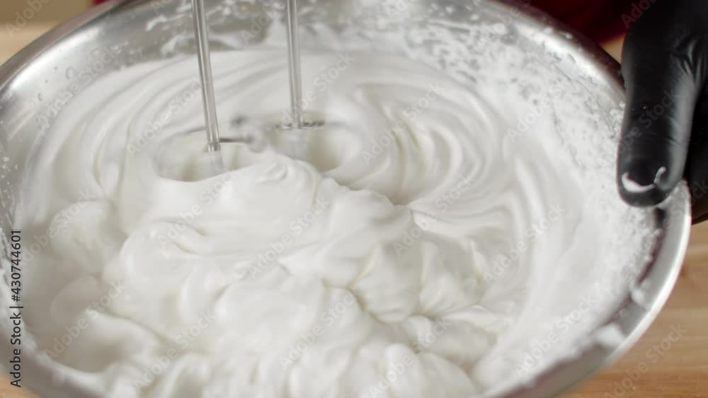 Male chef in black gloves whips egg whites with mixer in iron bowl in restaurant kitchen Male chef in black gloves whips egg whites with mixer in iron bowl in restaurant kitchen