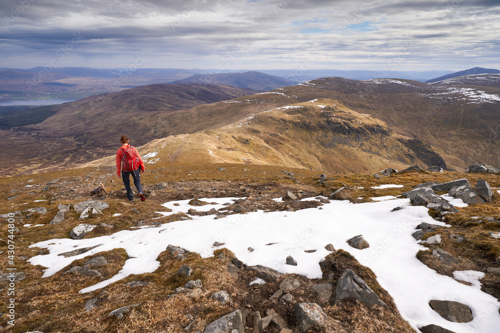 A hiker walking in the mountains towards the summits of An Sgorr and Meall Garbh from the summit of Carn Gorm in the winter. Scottish Highlands, UK Landscapes.