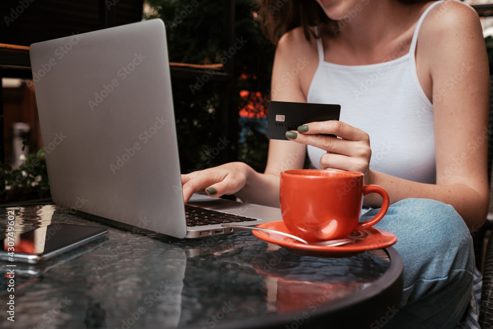 Young Woman Using Laptop and Holding Credit Card While Sitting in Cafe Outdoors, Online Shopping Concept Young Woman Using Laptop and Holding Credit Card While Sitting in Cafe Outdoors, Online Shopping Concept