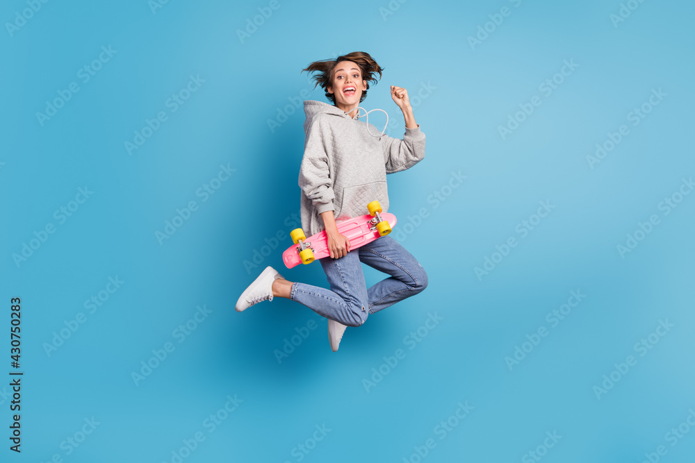 Full length body size photo of girl jumping up holding skate board gesturing like winner isolated vivid blue color background Full length body size photo of girl jumping up holding skate board gesturing like winner isolated vivid blue color background