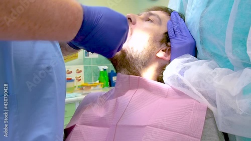 Team of dental surgeons performs surgery on teeth. in a modern clinic. Young dentist. Teamwork. Tooth doctor orthodontist surgeon doing medical operation on root canals. Stomatology office.