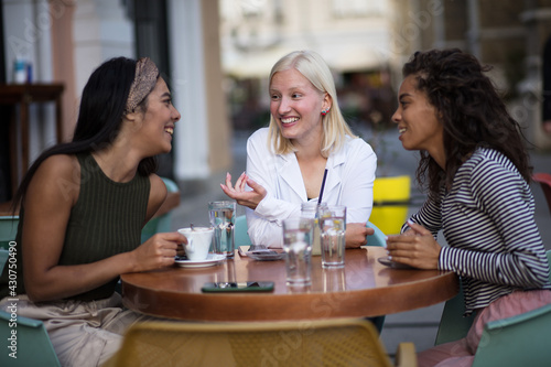 Three women sitting in café on street and talking.
