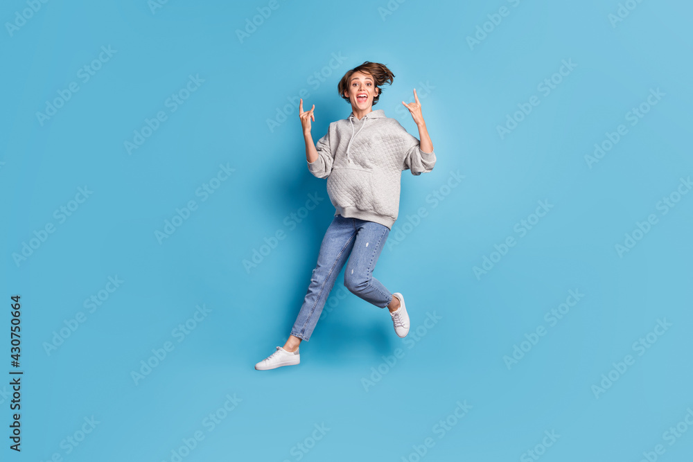 Full length body size side profile photo of girl jumping high showing heavy metal sign isolated vivid blue color background Full length body size side profile photo of girl jumping high showing heavy metal sign isolated vivid blue color background