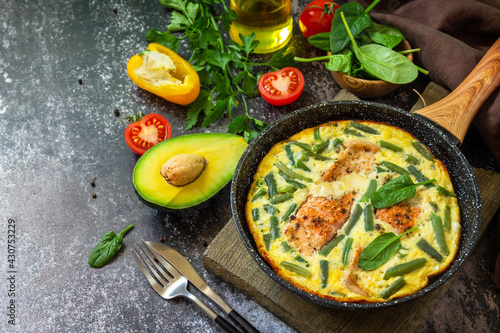 Breakfast or lunch snack concept. Rustic omelet (omelette, Scrambled)  with salmon fillet and green beans in a frying pan on a stone background. Copy space.