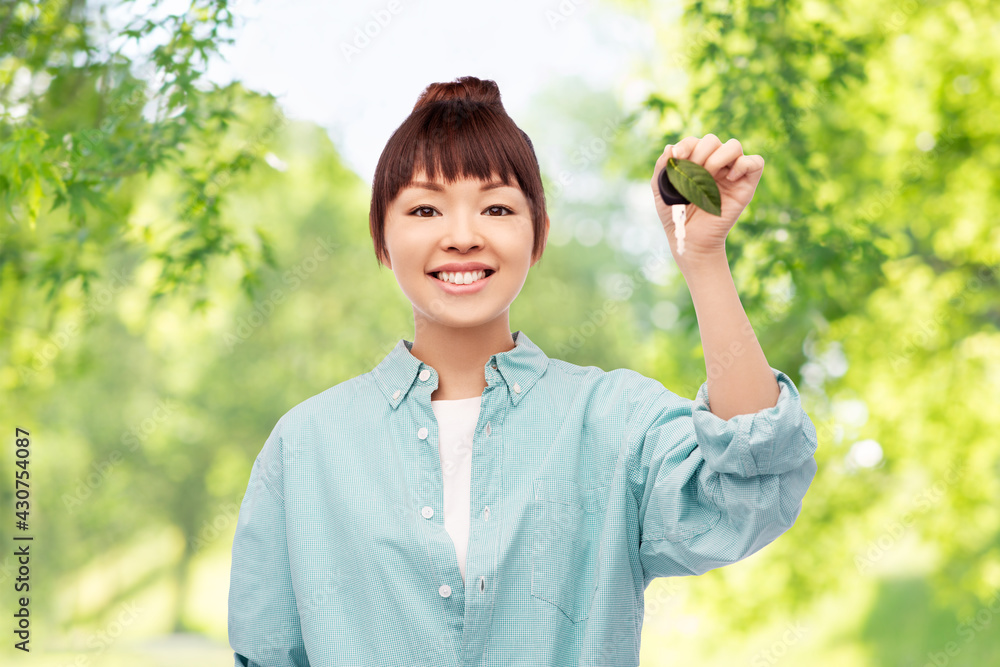 eco living, environment and sustainability concept - portrait of happy smiling young asian woman in turquoise shirt holding car key with green leaf over natural background eco living, environment and sustainability concept - portrait of happy smiling young asian woman in turquoise shirt holding car key with green leaf over natural background